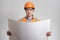 Man in builder`s uniform looking in opened project, holding large sheet of paper on grey background. Construction worker in