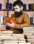 Man on busy thoughtful face reading book, bookshelves on background. Education and science concept. Teacher or student