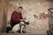 Man button up a dog collar against the background of a peeling wall. Portrait of man and white bull terrier. Dog trainer