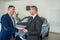 man buys an expensive car representative of car dealership shakes his hand as sign of agreement