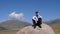 Man calling on phone while sitting on stone with Tian Shan mountains behind