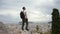 Man with camera stands on hill of old Greek city and raises hands on winning joy