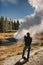 Man with a camera watching riverside geyser erupt