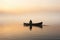 A man in canoe on a foggy tranquil lake at sunrise. Winter Autumn seasonal concept.