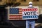 Man with cap blue jeans and medical mask holding a cardboard sign text VOTE with american stars and stripes flag on a wall in the