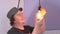 Man in cap screwing in a glass bulb, hanging from the top, with unprotected hand