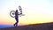 Man carries a bicycle of the mountain at sunset,slow mo