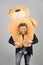 Man carries giant teddy bear on neck, grey background. Birthday gift concept. Teddy bear plush toy pleasant surprise