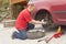 Man changing the punctured tyre on his car loosening the nuts with a wheel spanner before jacking up the vehicle.