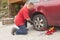 Man changing the punctured tyre on his car loosening the nuts with a wheel spanner before jacking up the vehicle.