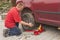 Man changing the punctured tyre on his car loosening the nuts with a wheel spanner before jacking up the vehicle.