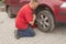 Man changing the punctured tyre on his car loosening the nuts with a wheel spanner before jacking up the vehicle.