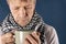 Man in a checkered scarf with big mug suffering from a sore throat and headache. Blue background