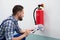 Man Checking Fire Extinguisher Writing On Document