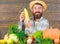 Man cheerful bearded farmer hold corncob or maize wooden background. Farmer straw hat presenting fresh vegetables