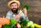 Man cheerful bearded farmer hold horseradish wooden background. Grow organic crops. Farmer straw hat presenting fresh