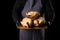 man chef in a striped blue apron and black clothes stands on a black background and holds a duck in his hand for cooking