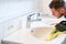 Man cleaning a bathroom sink with a scraper blade and micro fiber cloth to remove lime and stains