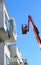 Man cleaning facade of a modern minimalistic apartment building on a telescopic boom lift using pressure jet wash with blue sky