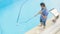 Man cleaning swimming pool with vacuum tube cleaner early in the morning.