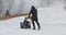 A man cleans the snow with a snowblower in yard at snowfall in slow motion