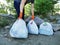 The man cleared the park and the beach from debris. He is holding bags of trash and plastic. The concept of teaching children to