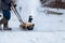 Man clears snow with a snow blower in house yard.