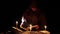 a man in a cloak with a hood is reading a hot book with candles on the floor