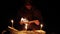 a man in a cloak with a hood is reading a hot book with candles on the floor