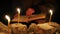 a man in a cloak with a hood is reading a hot book with candles on the floor