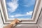 Man close new skylight mansard window in an attic room against blue sky.