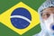 Man close-up in white protective suit, mask, glasses and gloves on the background of the flag of Brazil, coronavirus
