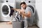 Man with clothes near washing machine. Handsome man sits in front of washing machine. Loads washer with dirty laundry