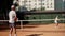 A man coach with a ward girl conduct a joint training tennis set at average intensity. The serving and deflecting blows
