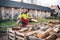 Man collects a pile of firewood on a heap. Coniferous and deciduous stacks of firewood. Industry and worker in concept of power an