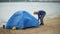 Man collects a tourist tent on the bank of the river of the sea