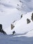 Man in colorful outfit skiiing down a very steep snow couloir under a cable car station in the Swiss Alps in deep winter