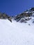 Man in colorful outfit skiiing down a very steep snow couloir under a cable car station in the Swiss Alps in deep winter