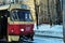 A man comes out from old red tram which stop in snowy street, building and park background