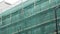 Man construction laborer in uniform works on scaffolding under green net