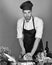 Man in cook hat and apron cuts cabbage. Cook works in kitchen near table with vegetables and tools