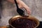 A man cook with a large spoon puts strawberry jam cooked in a copper basin into a glass jar.