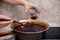 A man cook with a large spoon puts strawberry jam cooked in a copper basin into a glass jar.