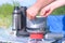 Man is cooking food using small gas burner in camping on nature, hands closeup.