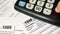 Man counting taxes on a calculator, documents on the table, tax form 1040 close up