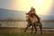 A man in cowboy costume on his horse in a corner against the sun against a background with rivers and mountains