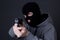 Man criminal in black mask aiming with gun over grey