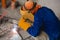 A man crouched and in full welding gear welds together a makeshift trowel, putty knife or scraper from two pieces of metal.