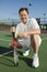 Man crouching on Tennis Court holding tennis racket and ball portrait