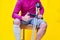 Man with crutches, jeans and purple shirt sitting on a chair with his thumb up, on yellow background